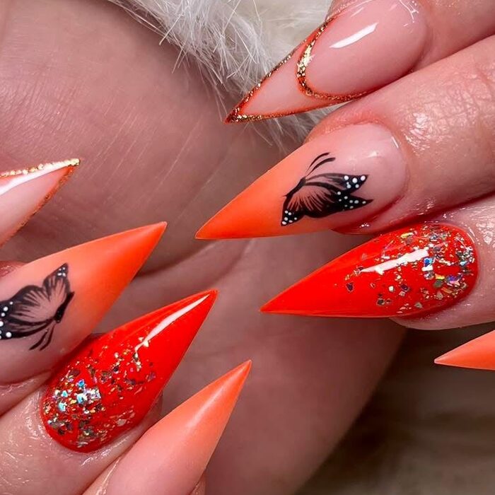 Orange stiletto nails with glitter and butterflies