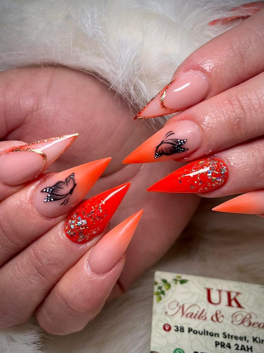 Orange stiletto nails with hand-painted butterflies, done at UK Nails & Beauty